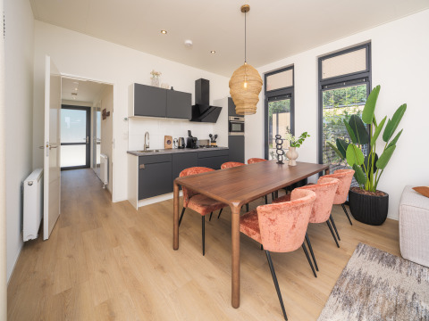 Interior de lodge moderno con cocina, comedor y grandes ventanales en Essenburgh Deluxe, Veluwepark de Bosgraaf, NL.