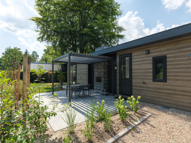 Lodge moderno en Veluwepark de Bosgraaf, Países Bajos, con patio, jardín y pérgola bajo cielo azul claro.