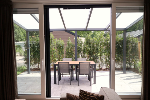 Vista dal soggiorno sul patio con tavolo da pranzo e quattro sedie al Rosendael Comfort met hottub, Veluwepark de Bosgraaf, Paesi Bassi.