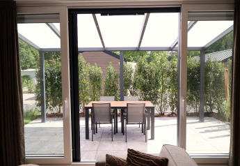 View from the living room to patio with dining table and four chairs at Rosendael Comfort met hottub, Veluwepark de Bosgraaf, Netherlands.
