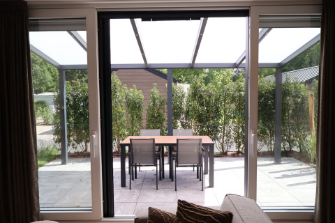 Zicht vanuit de woonkamer op terras met eetafel en vier stoelen bij Rosendael Comfort met hottub, Veluwepark de Bosgraaf, Nederland.