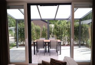 Zicht vanuit de woonkamer op terras met eetafel en vier stoelen bij Rosendael Comfort met hottub, Veluwepark de Bosgraaf, Nederland.