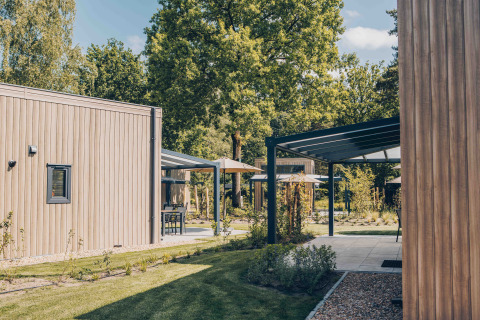 Buitenaanzicht van Reeëndal Lodge Comfort in Veluwepark de Bosgraaf, Nederland, met moderne chalets en natuur.