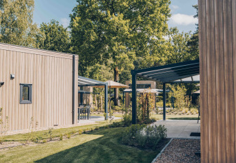 Vista exterior de Reeëndal Lodge Comfort en Veluwepark de Bosgraaf, Países Bajos, con cabañas modernas y vegetación.