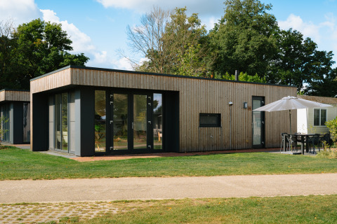 Modern Happy Oak Lodge with large glass windows, wood siding, and outdoor seating under a patio umbrella.