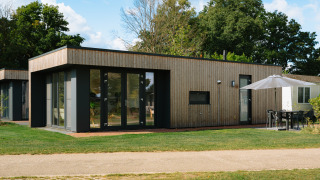 Happy Oak Lodge moderne avec grandes baies vitrées, façade en bois et salon de jardin sous un parasol.