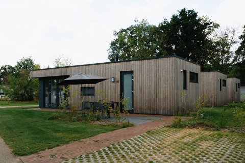 Modern wooden lodge at Happy Oak Lodge, Holiday Park Mölke, featuring patio seating and green surroundings.