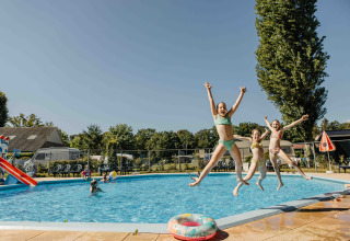 Tres niños se lanzan alegres a una piscina en un alojamiento glamping, disfrutando de un día soleado.