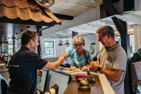 Et ældre par tjekker ind på en glamping-indkvartering og hilser venligt på receptionisten.
