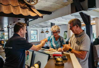 Et ældre par tjekker ind på en glamping-indkvartering og hilser venligt på receptionisten.