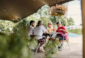 Eine Familie sitzt unter einem Zelt beim Glamping, trinkt und isst an einem gedeckten Tisch im Freien.