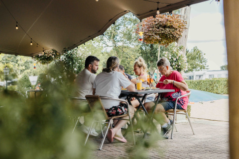 Een familie geniet samen van een maaltijd en drankjes onder een tent op een glampingverblijf.