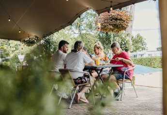 Eine Familie sitzt unter einem Zelt beim Glamping, trinkt und isst an einem gedeckten Tisch im Freien.