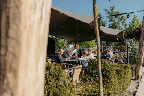 Buitencafé bij een glampingverblijf waar mensen in het zonnetje onder een luifel zitten te ontspannen.