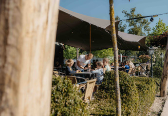 Area caffè all'aperto presso una struttura glamping con persone sedute sotto una tenda in giornata di sole.