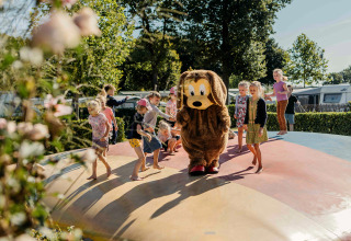 Children play on an inflatable pillow at a glamping site, joined by a person in a dog costume on a sunny day.