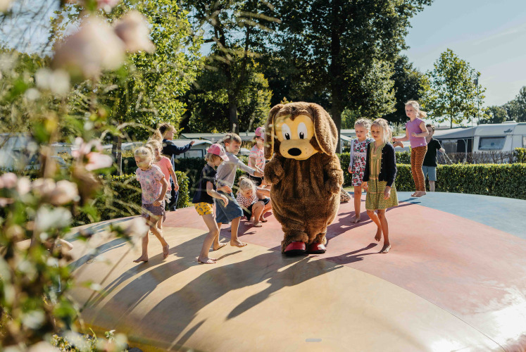 Niños juegan en un cojín inflable en un alojamiento glamping, acompañados de alguien disfrazado de perro.