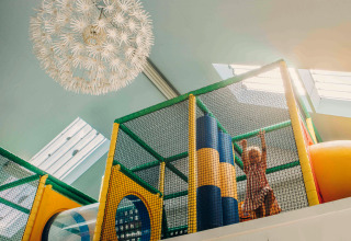Child playing in a colorful indoor play area at a glamping accommodation, with sunlight streaming in above.