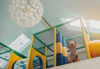 Niño jugando en una colorida área de juegos interior dentro de un alojamiento glamping, con luz natural arriba.
