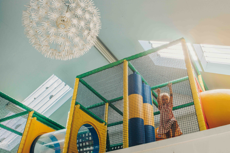 Niño jugando en una colorida área de juegos interior dentro de un alojamiento glamping, con luz natural arriba.