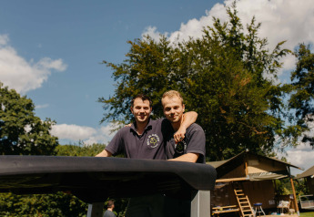 Due uomini con polo scure sorridono insieme all'aperto in un alloggio glamping in una giornata soleggiata.