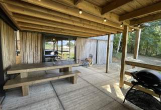 Terraza cubierta con mesa de madera, bancos y barbacoa en una tiny house en el bosque de Limburg, Bélgica.