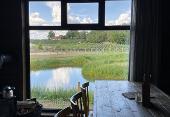 Zicht vanuit een tiny house met houten tafel op vijver, groene velden en wijngaarden in Limburg, België.