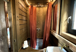 Baño pequeño con paredes de madera, tina de metal y cortinas rojas en Shelter + jacuzzi, Cosy Cabins, Limburg.