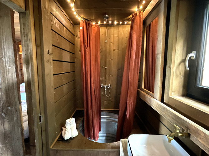 Tiny house bathroom with wooden walls, metal tub, and red curtains at Shelter + jacuzzi, Cosy Cabins, Limburg.
