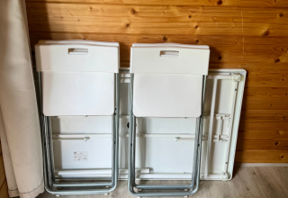 Due sedie pieghevoli appoggiate contro una parete in legno in una cabina, con un tavolo piegato dietro.