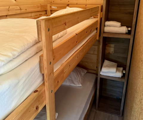 Literas de madera con sábanas limpias y estantes con toallas en una cabaña básica en Urban-Gardens Ieper.