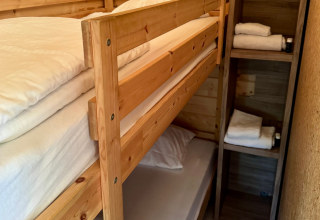 Literas de madera con sábanas limpias y estantes con toallas en una cabaña básica en Urban-Gardens Ieper.