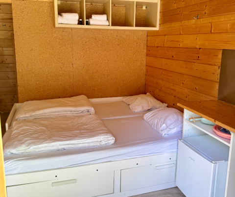 Slaapkamer in een basic blokhut bij Urban-Gardens Ieper met een tweepersoonsbed en kleine koelkast.