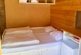 Kamer in een eenvoudige blokhut bij Urban-Gardens Ieper met tweepersoonsbed, handdoeken en frigo.