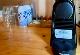Cafetera con tazas y vasos en una mesa de madera dentro de una cabaña en Urban-Gardens Ieper, Bélgica.