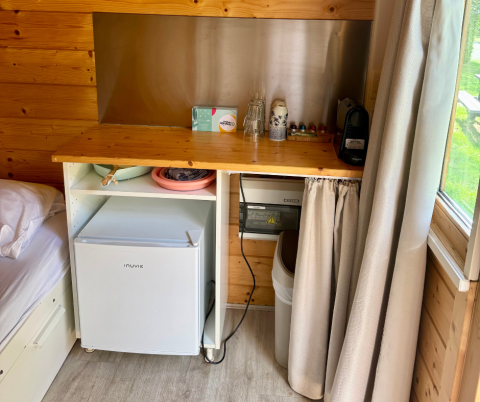 Rincón de cocina en cabaña con mini nevera y cafetera en Urban-Gardens Ieper, Bélgica, junto a ventana.