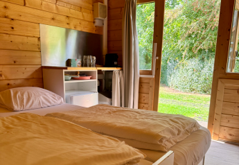 Interieur van een eenvoudige blokhut met tweepersoonsbed, houten muren en tuinzicht in Ieper, België.