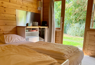 Interieur van een eenvoudige blokhut met tweepersoonsbed, houten muren en tuinzicht in Ieper, België.