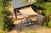 Four people enjoy an outdoor meal at a picnic table beside the Sand Lodge Jacuzzi tiny house with sunshade.