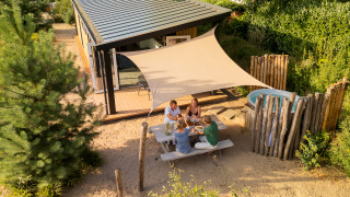 Vier mensen genieten van een maaltijd buiten bij de Sand Lodge Jacuzzi tiny house onder een zonnedoek.