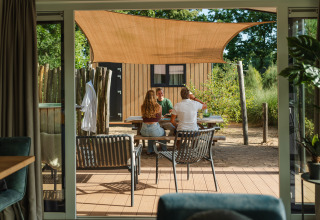 Trois personnes attablées sous une voile d’ombrage à Sand Lodge Jacuzzi, Holiday Park De IJsvogel, Pays-Bas.