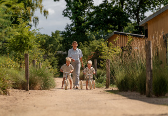 Erwachsener und zwei Kinder spielen auf einem Weg am Sand Lodge Jacuzzi im Holiday Park De IJsvogel, Niederlande.