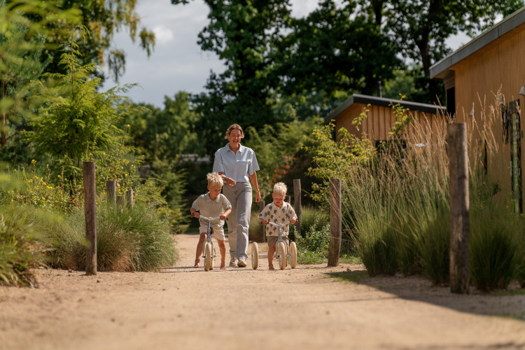 Erwachsener und zwei Kinder spielen auf einem Weg am Sand Lodge Jacuzzi im Holiday Park De IJsvogel, Niederlande.