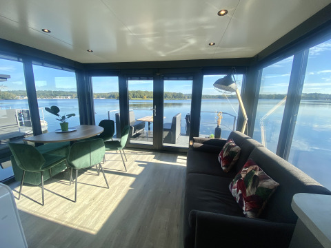 Salón moderno de una casa flotante en Marina Mookerplas, Países Bajos, con vistas al lago y grandes ventanales.