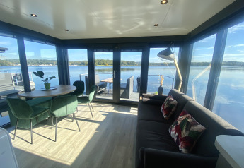 Salón moderno de una casa flotante en Marina Mookerplas, Países Bajos, con vistas al lago y grandes ventanales.