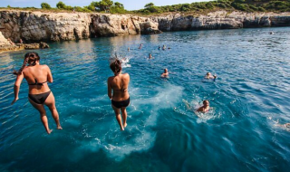 Folk hopper i havet fra klipper i nærheden af Medulin, Istrien, Kroatien, omgivet af svømmere.