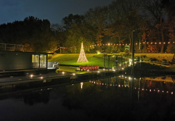 Beleuchteter Weihnachtsbaum und Lichterketten bei Nacht, gesehen vom Hausboot Marina Mookerplas, Niederlande.