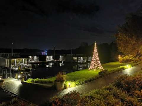 Foto nocturna en un alojamiento glamping junto al agua con cabañas flotantes y árbol de Navidad iluminado.