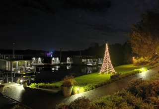 Foto nocturna en un alojamiento glamping junto al agua con cabañas flotantes y árbol de Navidad iluminado.