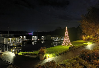 Foto nocturna en un alojamiento glamping junto al agua con cabañas flotantes y árbol de Navidad iluminado.